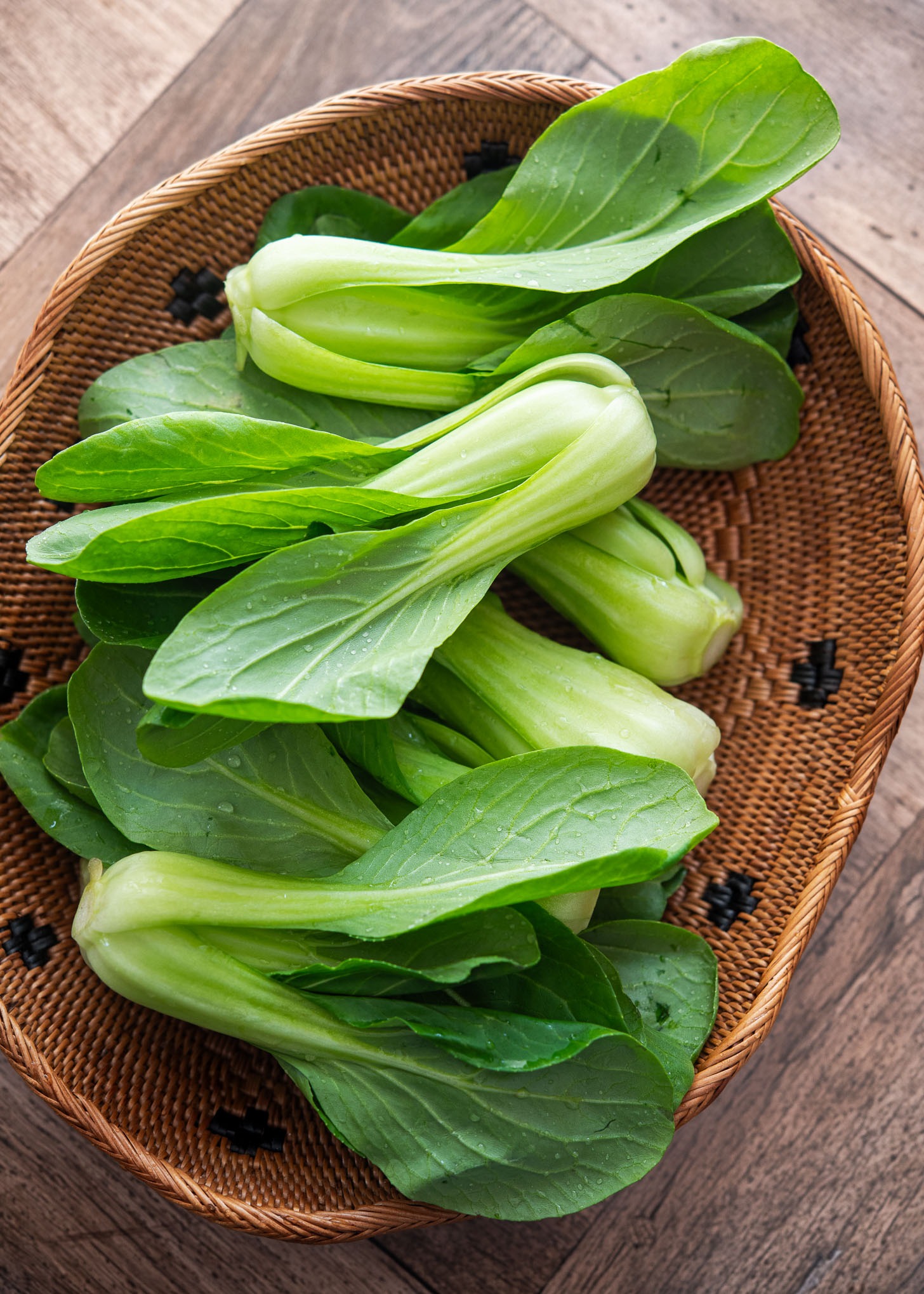 Fresh Shanghai bok choy with crisp green leaves and pale stems in a woven basket.