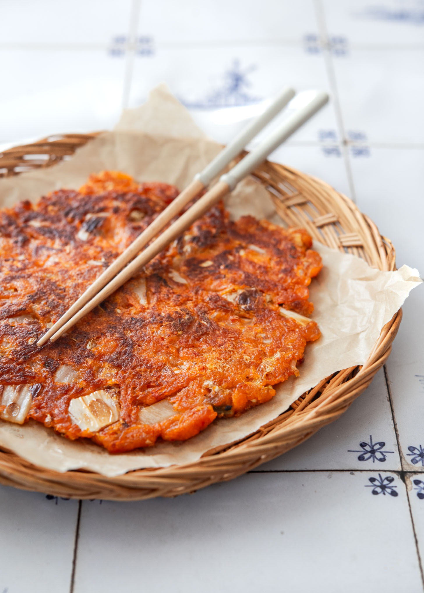 Crispy kimchi pancake with chopsticks on a serving dish.