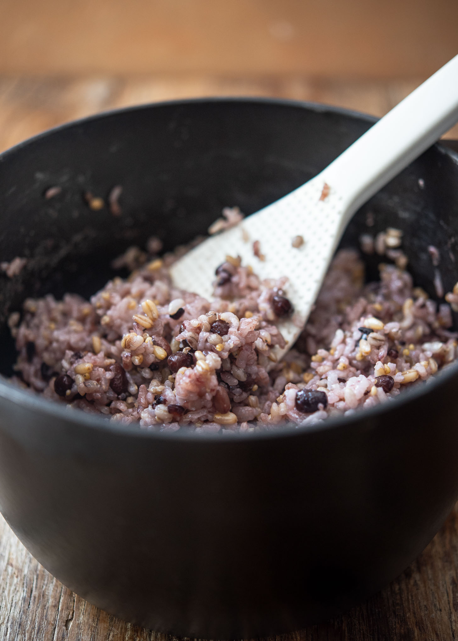 Rice paddle scooping japgokbap (Korean multigrain rice) from a cooking pot.