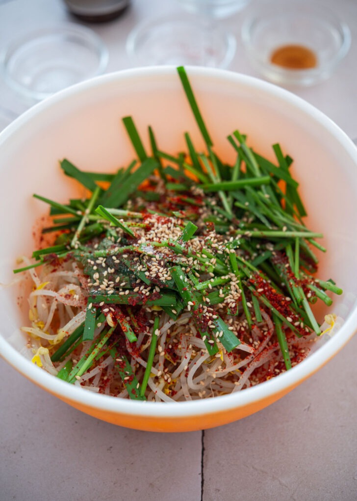 Mixing blanched mung bean sprouts and Asian chives with seasoning for noodle topping.