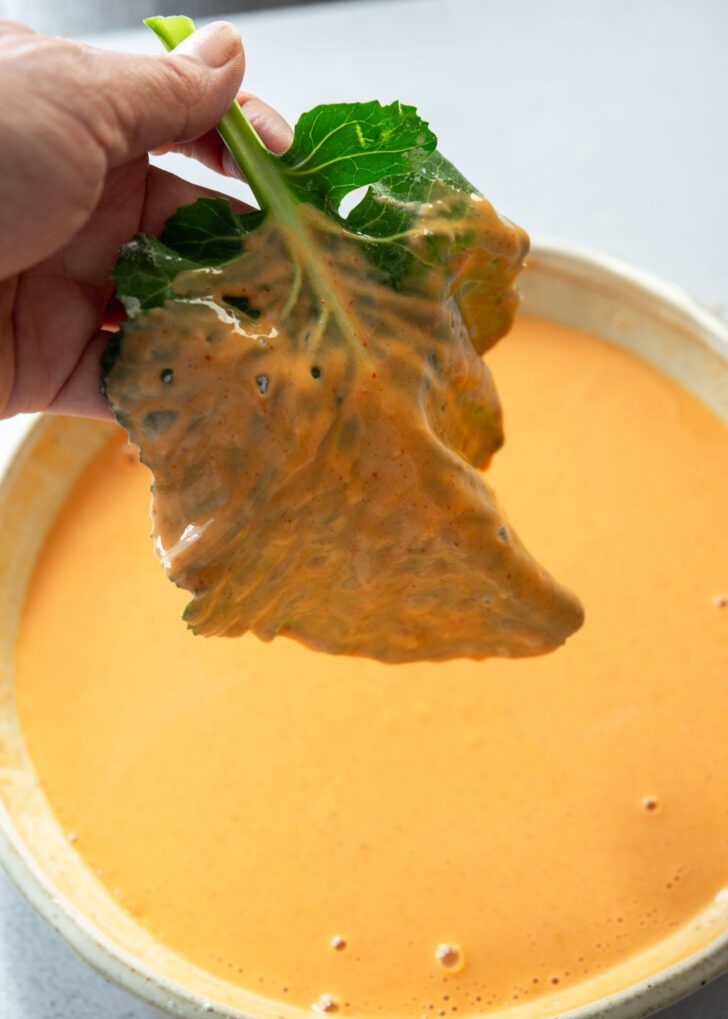 Kale leaf being coated in gochujang pancake (jangtteok) batter