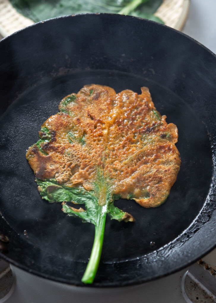 Golden brown kale gochujang pancake (jangtteok) cooked in a skillet