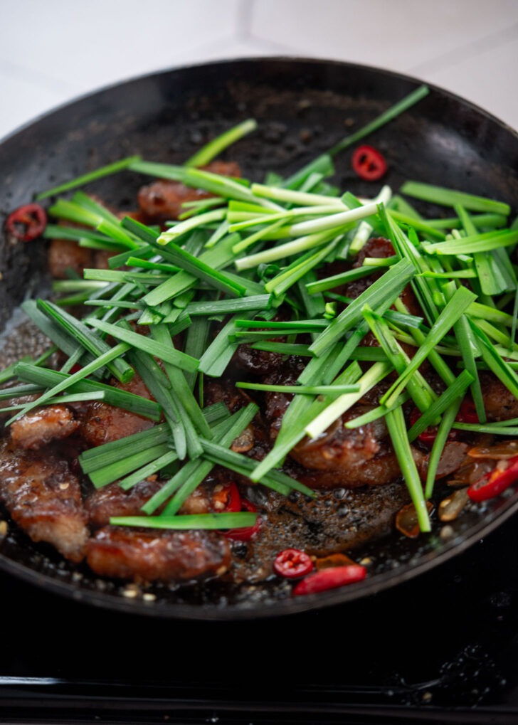 Fresh chives being added to honey garlic pork in the final step
