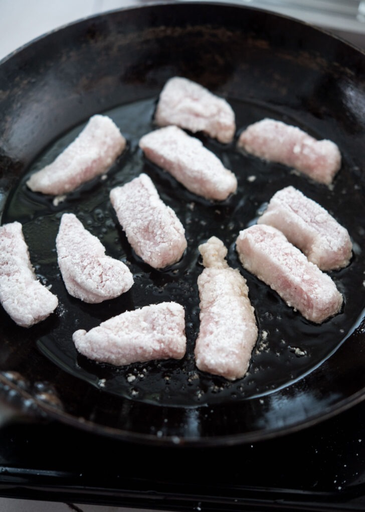 Starch-coated pork pieces added to a hot skillet with oil