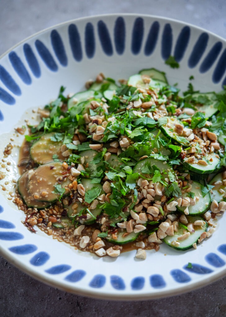 Creamy peanut dressing poured over sliced cucumbers in a mixing bowl
