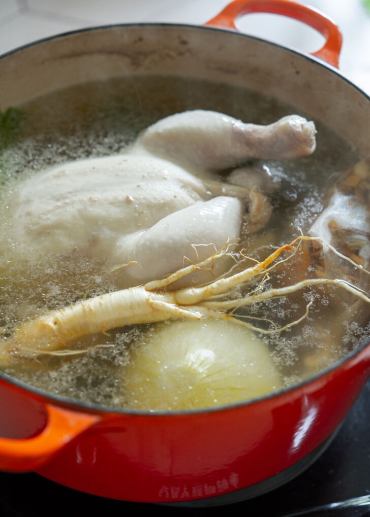 Simmering whole stuffed chicken with herbs and aromatics in a pot