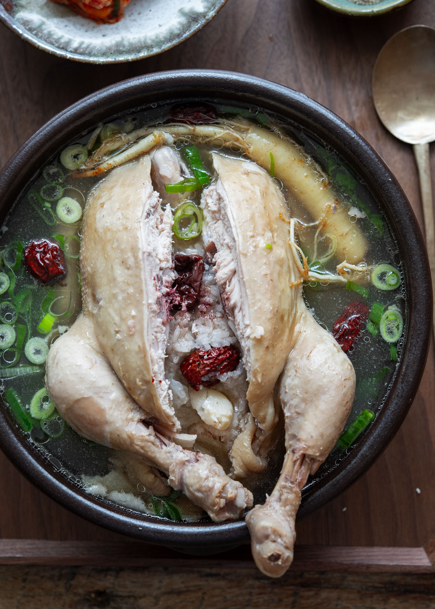 Samgyetang with whole chicken in broth, cut open to reveal glutinous rice stuffing

