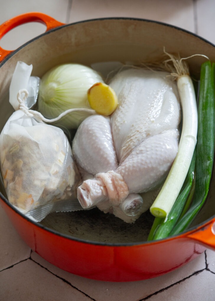 Adding stuffed chicken, herbal pack, and aromatics to a pot of water