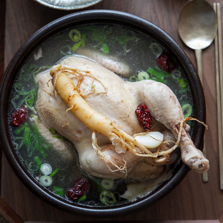 Samgyetang (Korean whole chicken soup) garnished with ginseng in a serving bowl