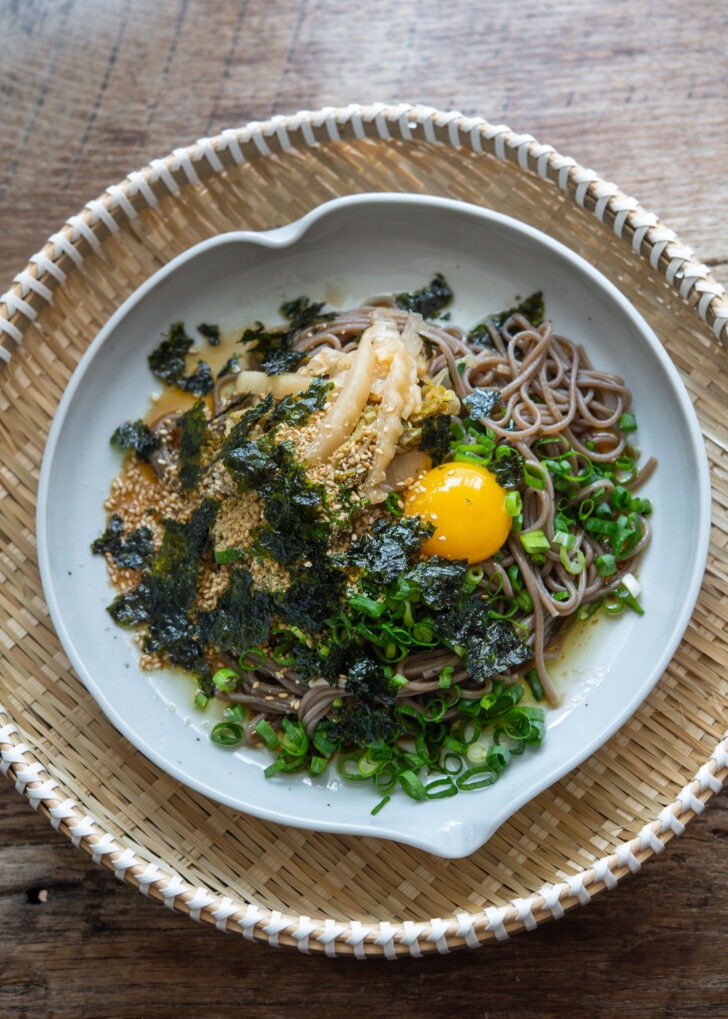 Makguksu topped with kimchi, green onion, egg, yolk, crumbled seaweed and sesame seeds,