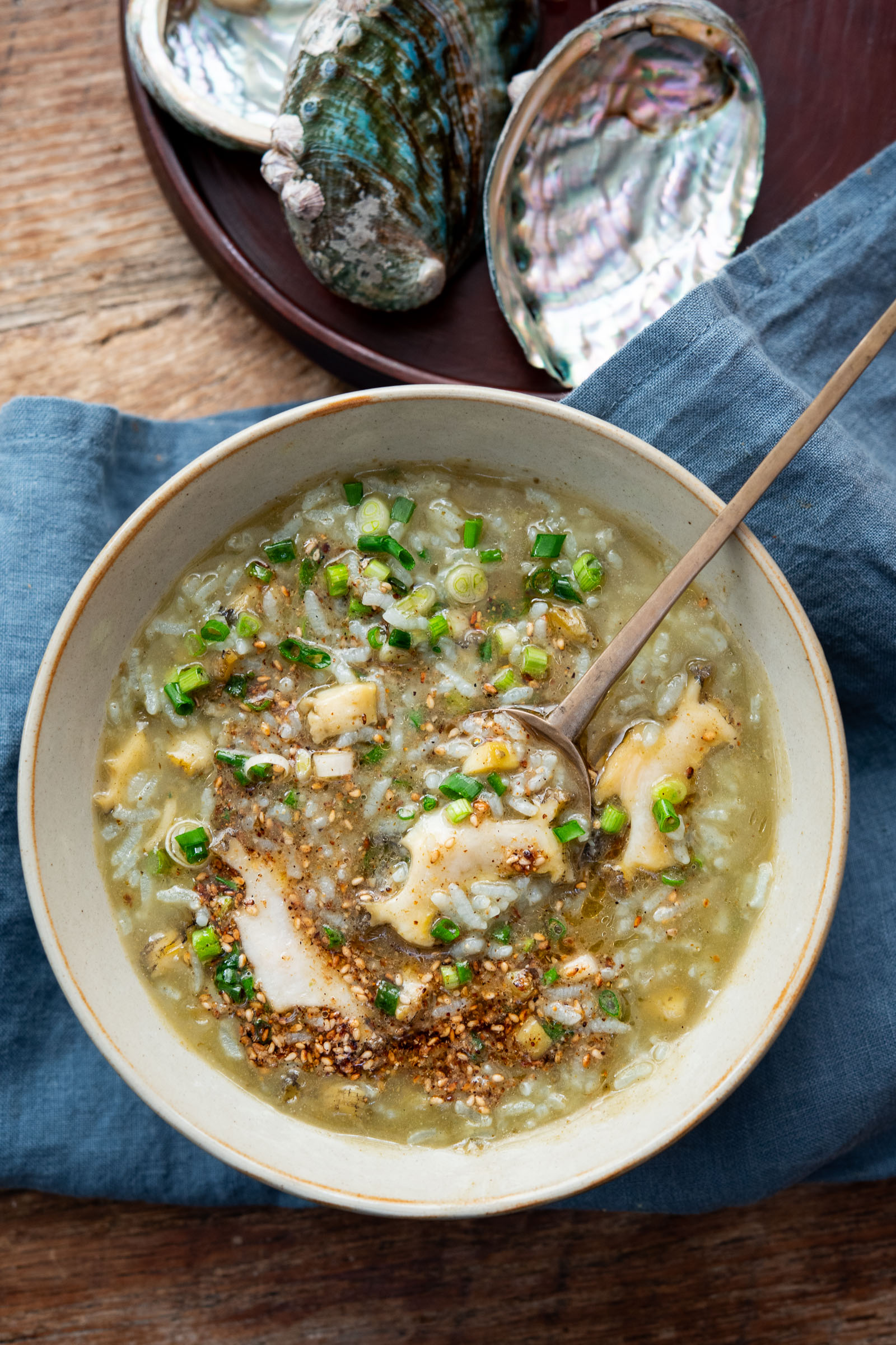 A spoonful of jeonbokjuk (abalone porridge) garnished with green onion and sesame seeds in a bowl