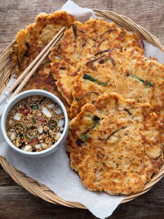 Crispy Korean bindaetteok arranged in a basket with soy dipping sauce and chopsticks