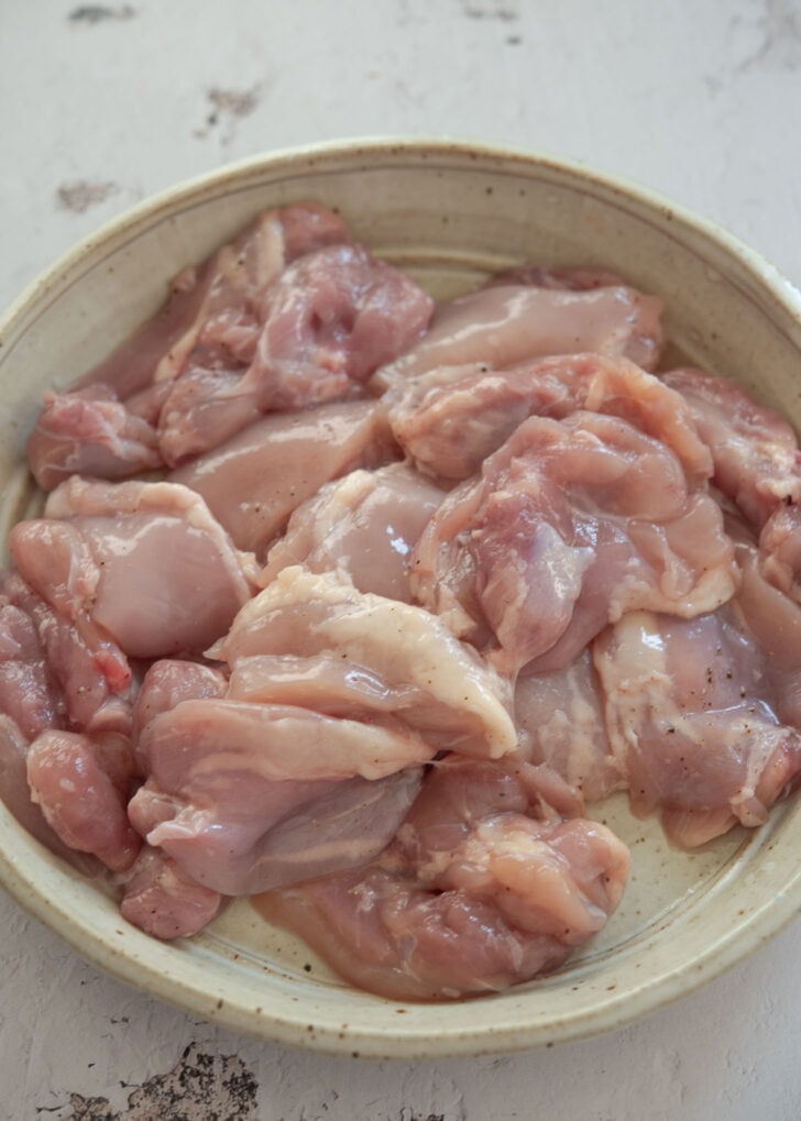Boneless chicken thighs seasoned with salt, pepper, and rice wine in a bowl