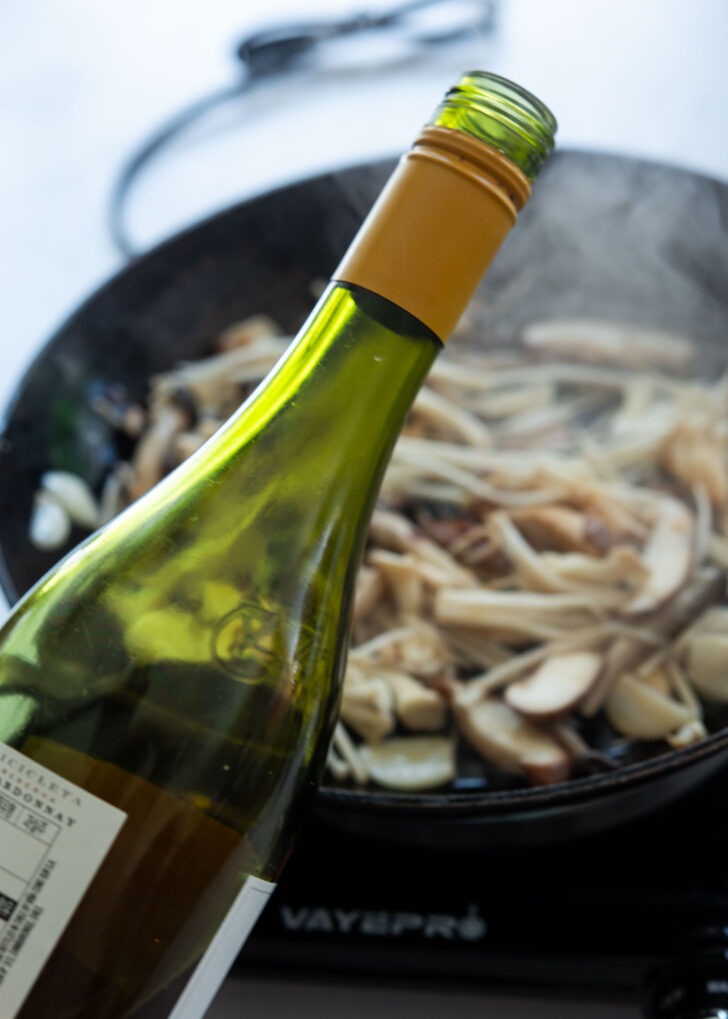 White wine poured over sautéed mushrooms in a skillet

