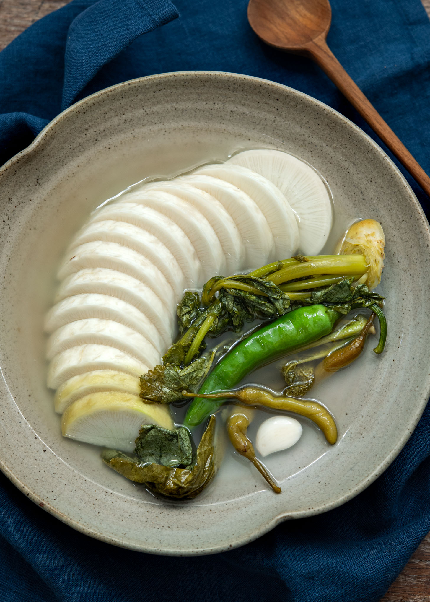 Bowl of sliced radish water kimchi with greens in clear, chilled brine