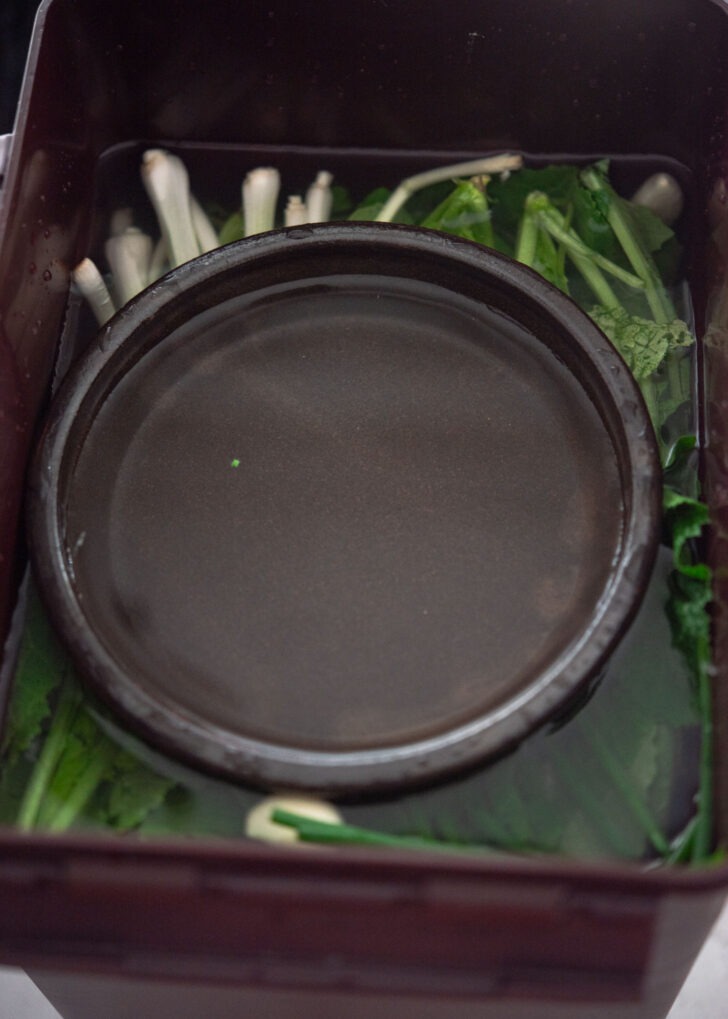 A heavy bowl placed on top of the greens to keep everything submerged