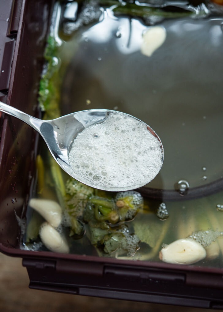 Spoon removing foam from dongchimi brine