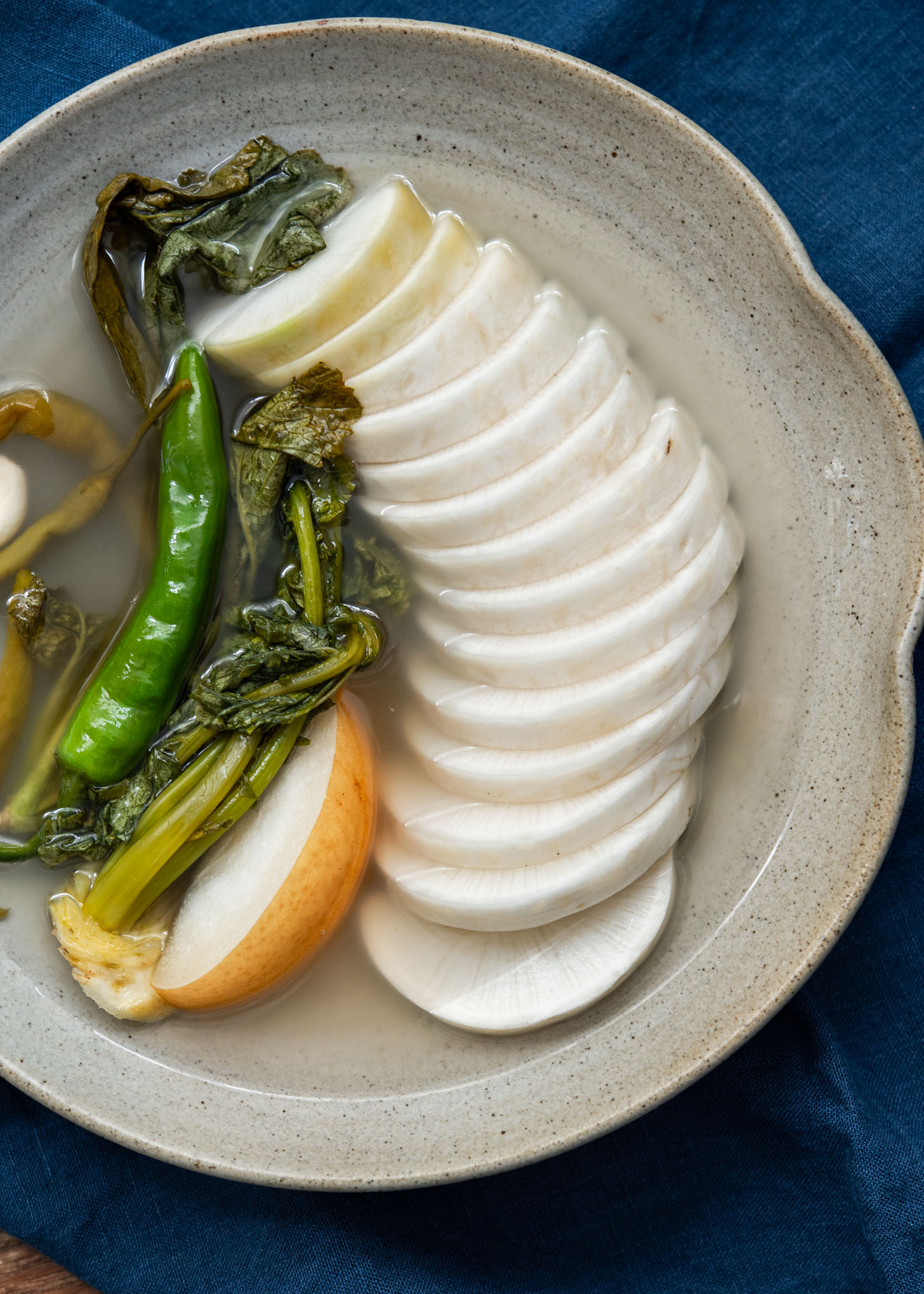Dongchimi served in clear chilled brine with sliced Korean radish and greens