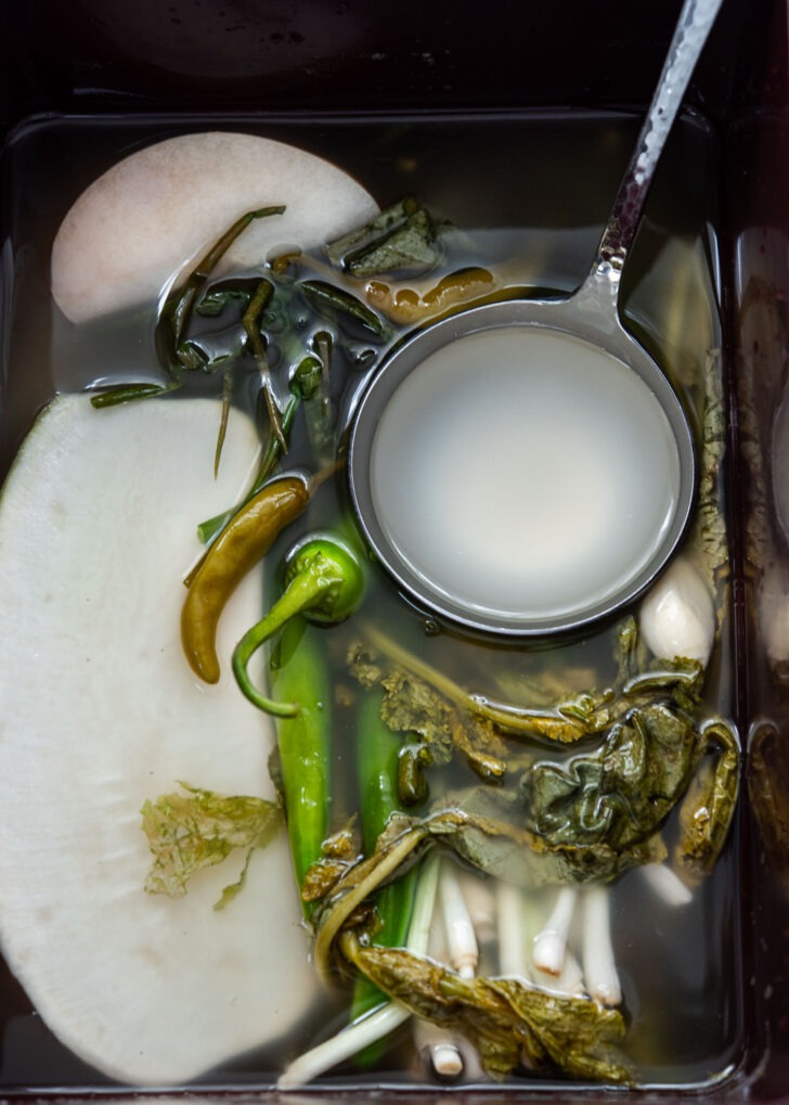 Ladle holding clear dongchimi brine in radish water kimchi