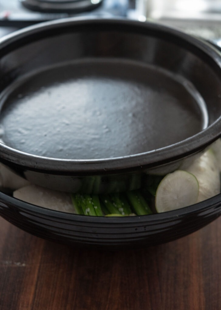 Stone bowl weighing down salted radishes