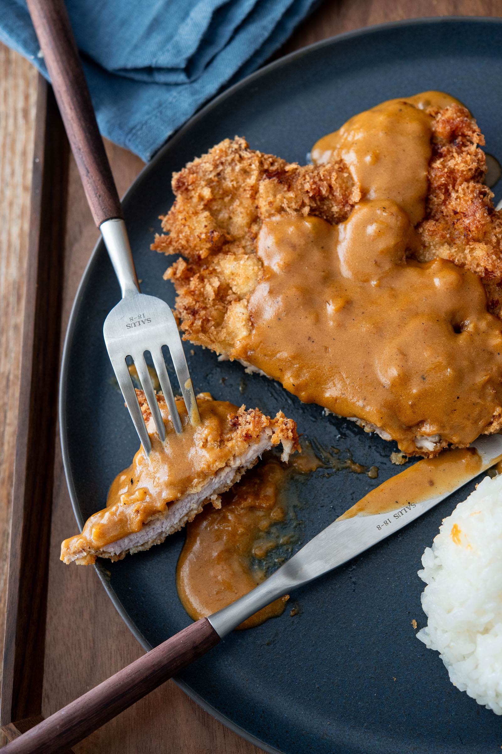 Korean donkatsu pork cutlet with brown sauce being cut with a fork and knife