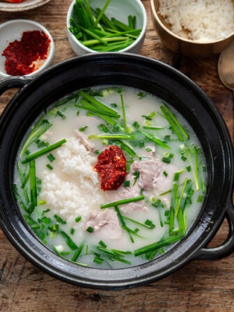 A comforting bowl of Busan-style pork rice soup topped with spicy dadaegi and fresh garlic chives.