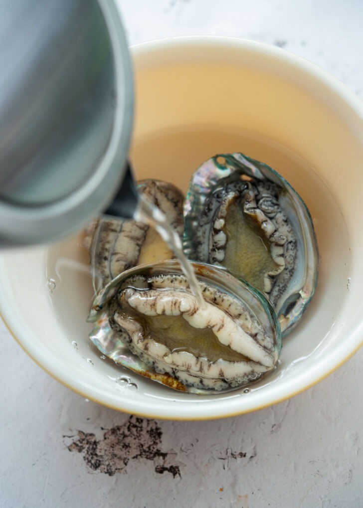 Pouring how water over fresh abalones in a bowl