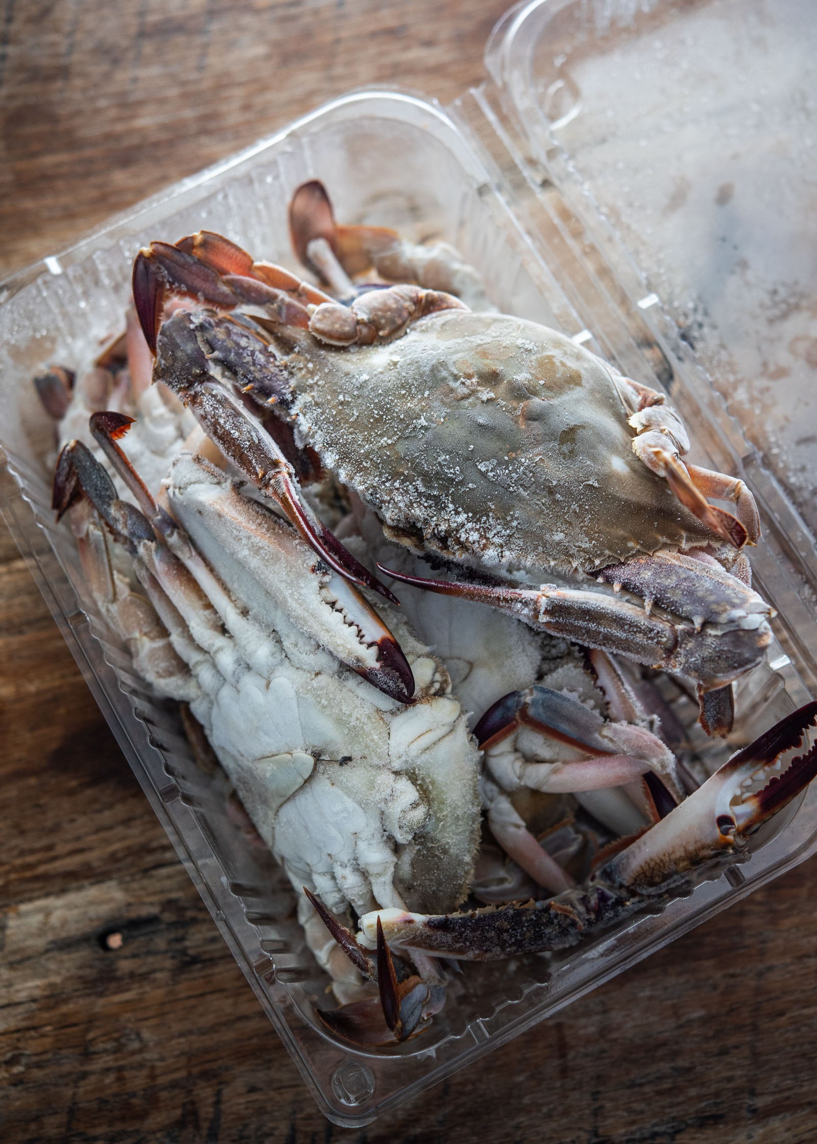 Whole frozen crabs in a clear plastic tray.