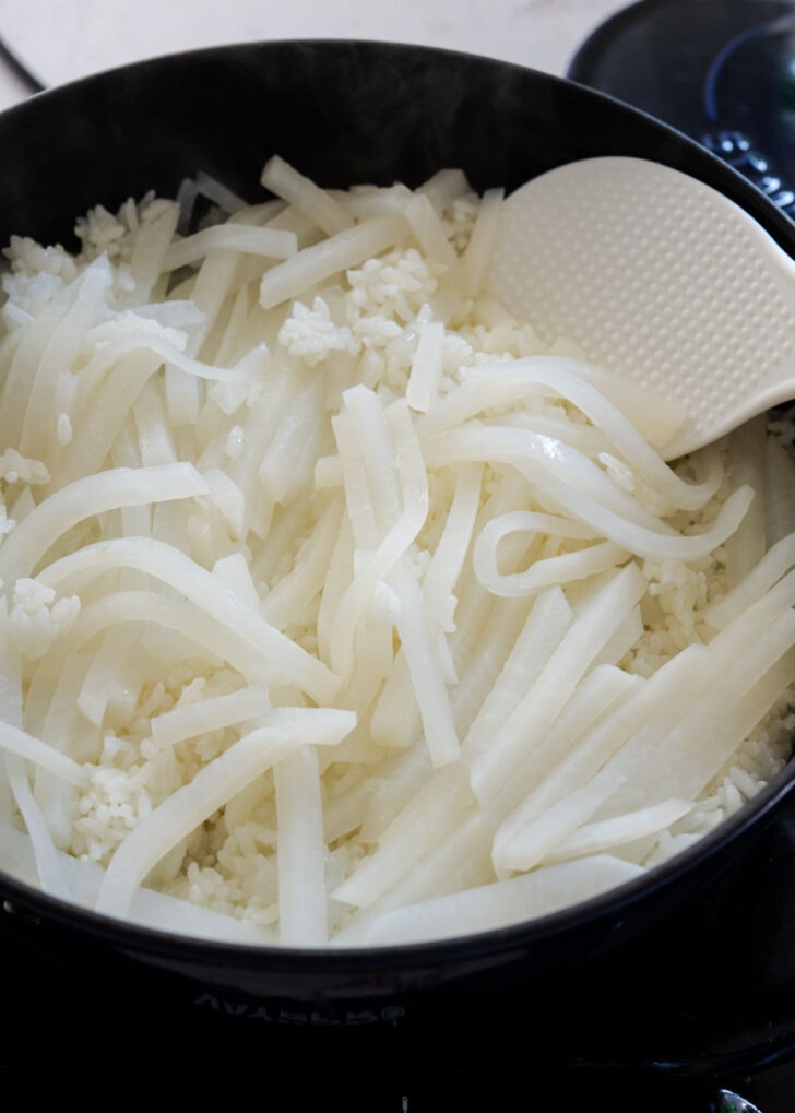 Rice paddle gently tossing cooked radish rice in a pot