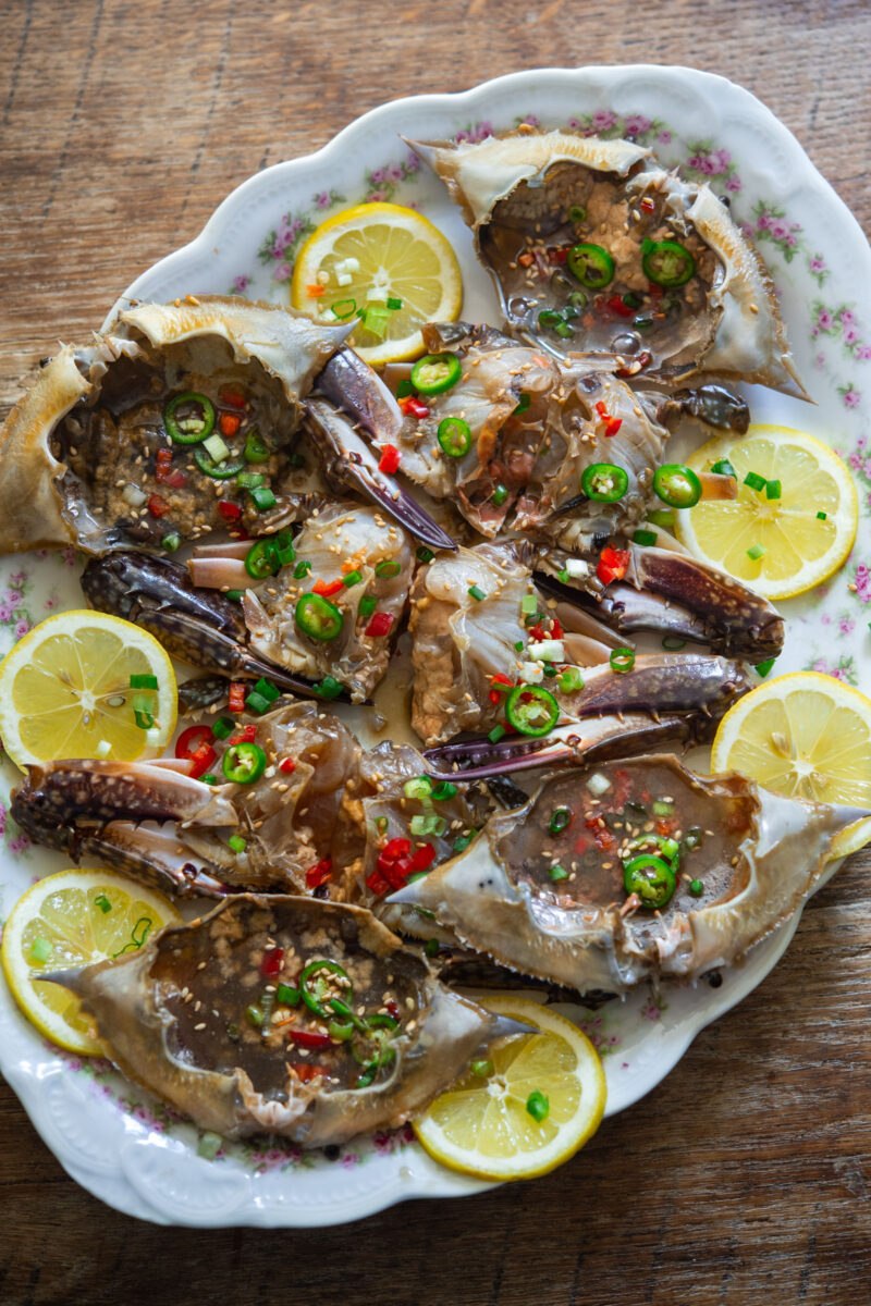 Ganjang gejang on an oval platter with lemon slices, green onions, and chopped chilies.