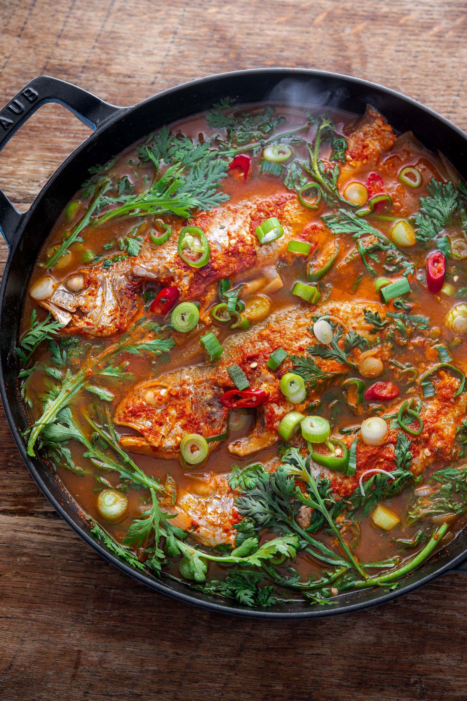 Korean fish stew (maeuntang) with croaker, radish, and fresh herbs in a spicy red broth
