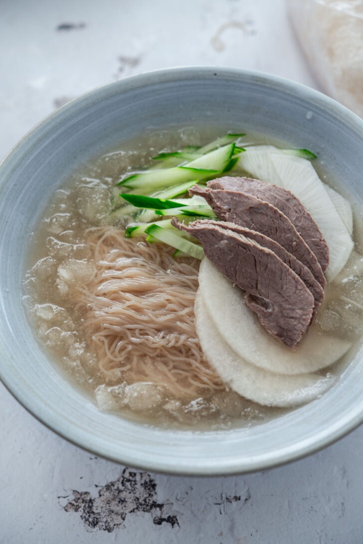 Assembling a bowl of mul-naengmyeon with toppings