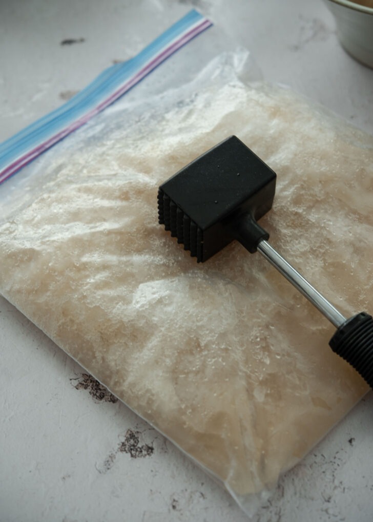 Breaking frozen naengmyeon broth in a bag with a hammer