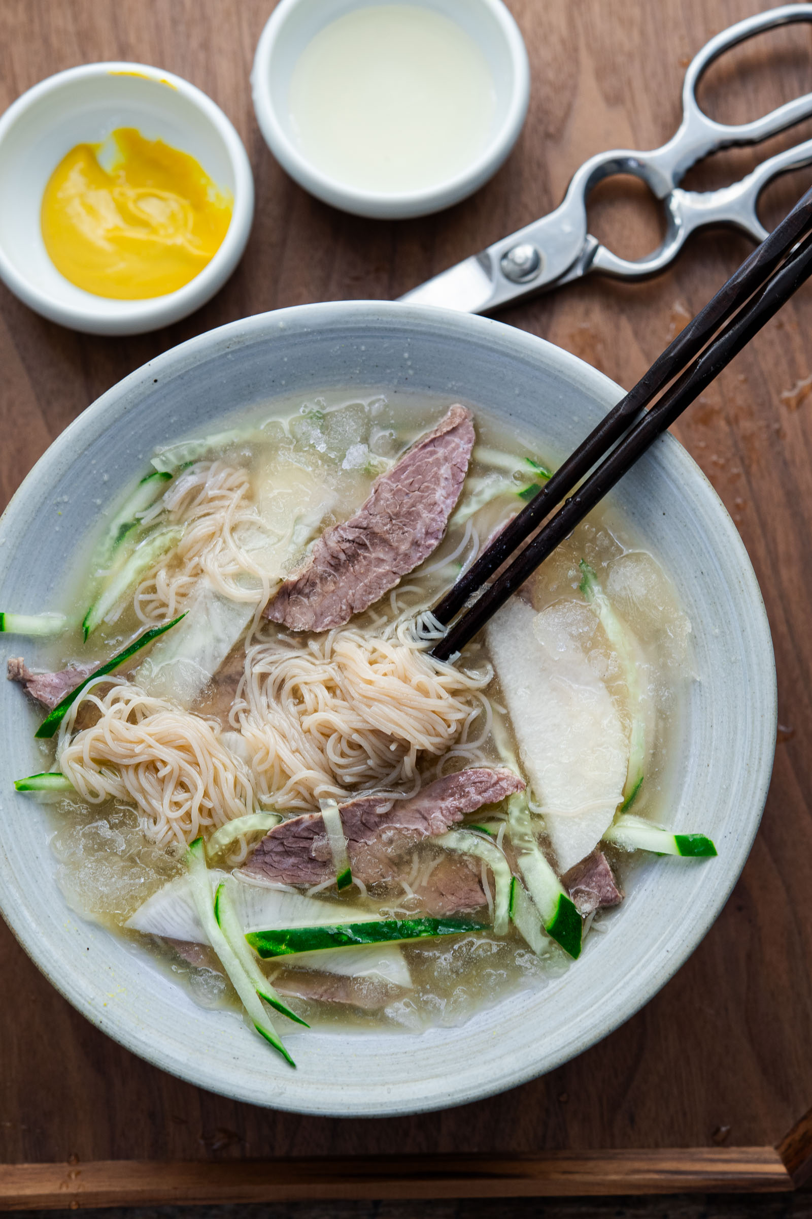 mul naengmyeon with noodles lifted by chopsticks in icy broth with beef and radish