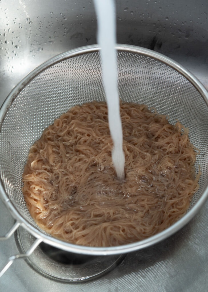 Rinsing cooked naengmyeon noodles under the cold water