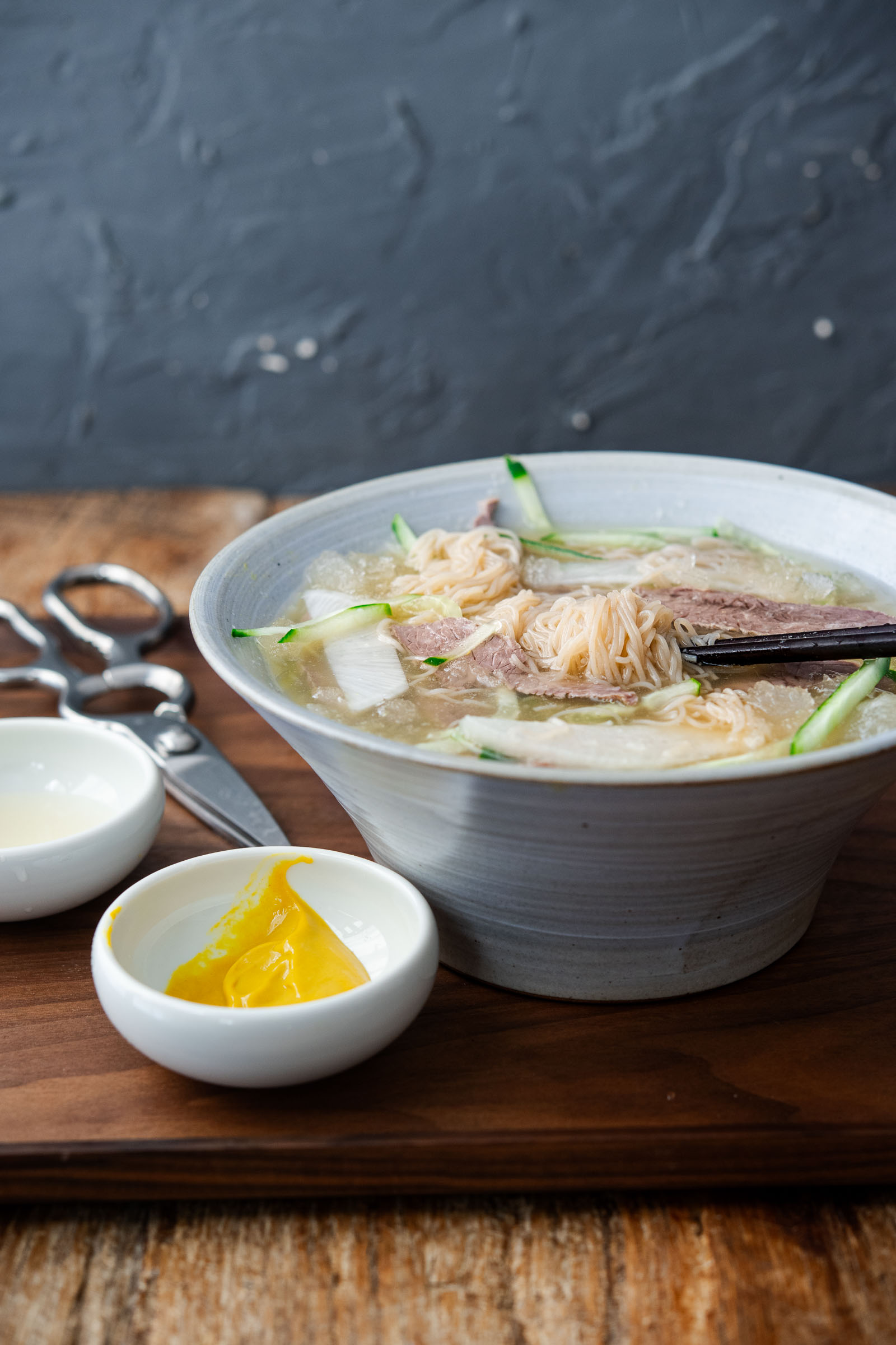 mul naengmyeon korean cold noodle soup with beef, noodles, and icy broth on a wooden tray