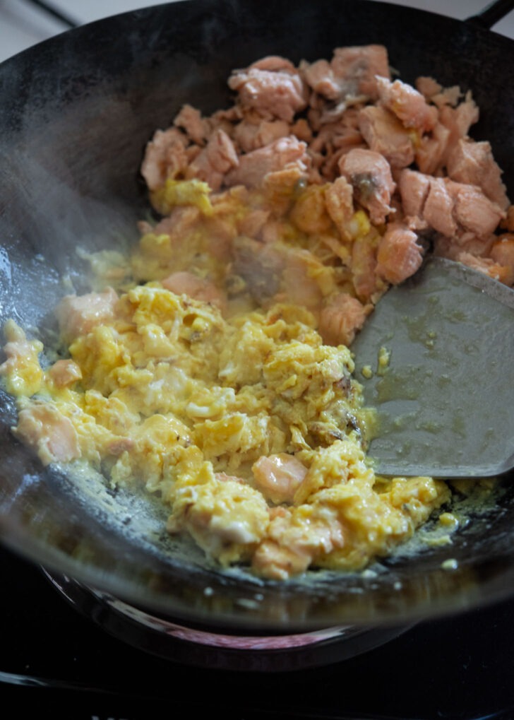 Egg scrambled next to salmon in a wok