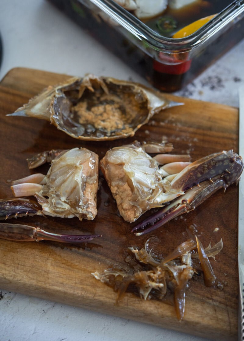 Soy-marinated crab cut in half on a wooden board, with the top shell set aside.