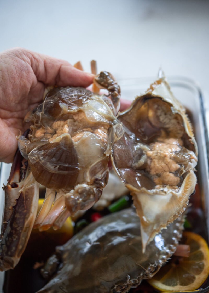 Lifting the top shell from a soy-marinated crab to reveal the meat and innards.