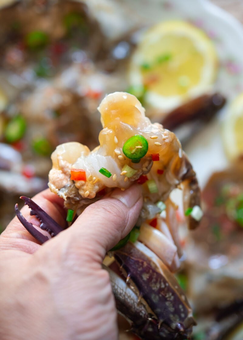 Squeezing tender soy-marinated crab meat from the shell, topped with green onion and chili.