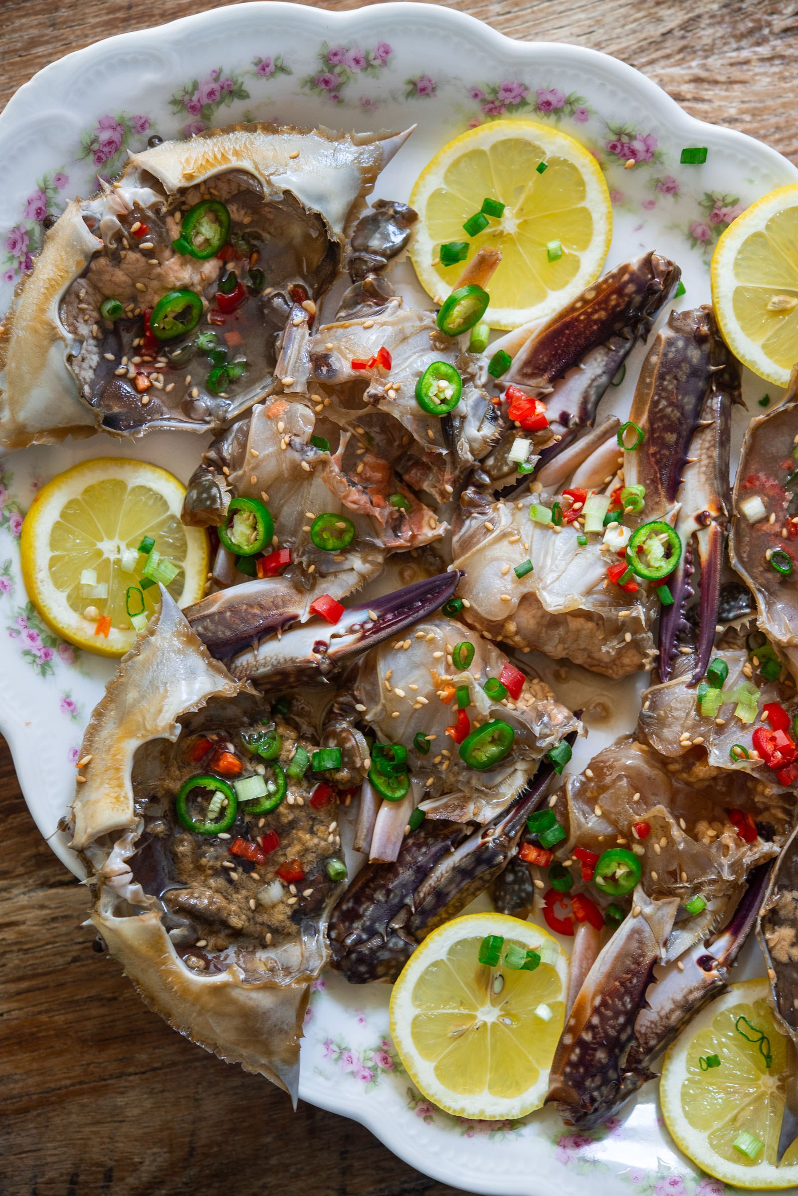 Cut soy-marinated
crabs on a platter with lemon slices, green onions, and red chilies.