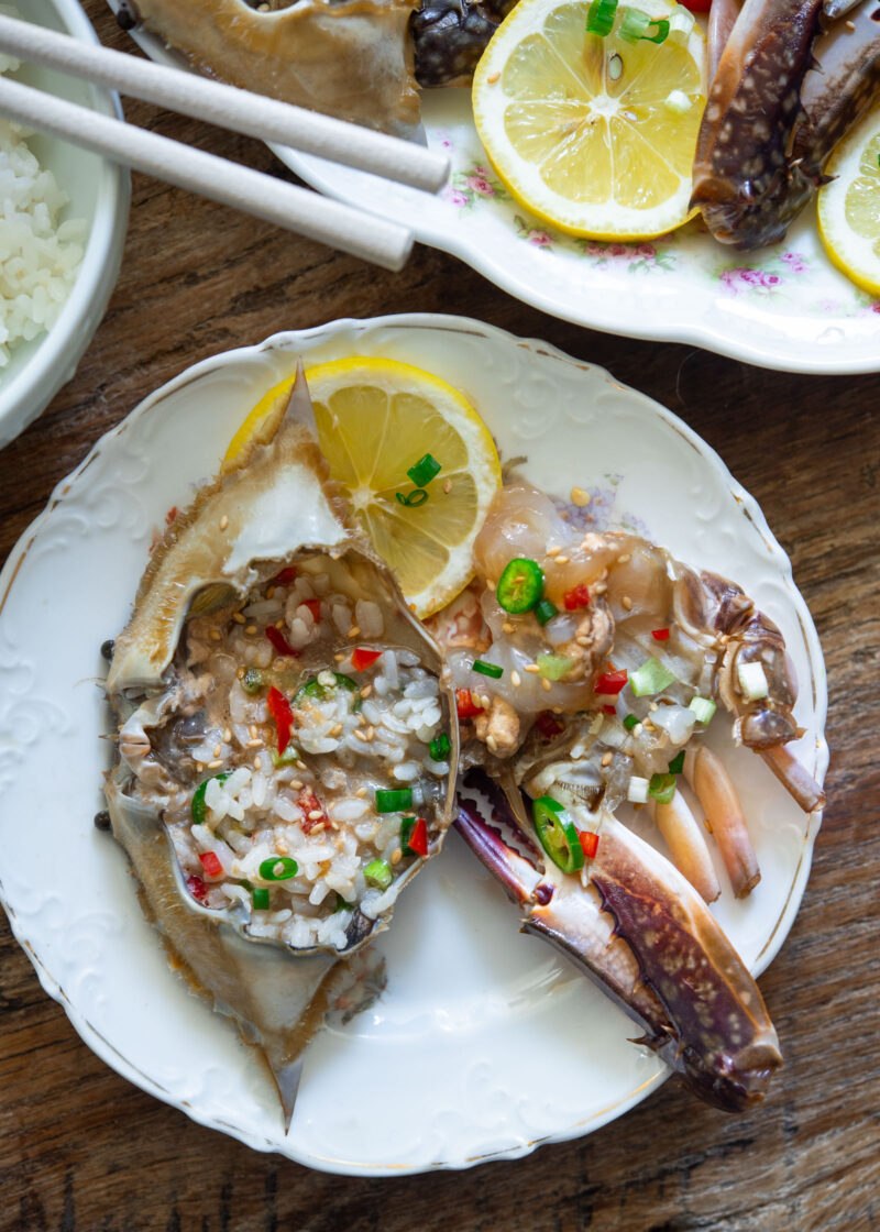 Rice mixed with soy marinade inside a crab shell, served beside marinated crab pieces.