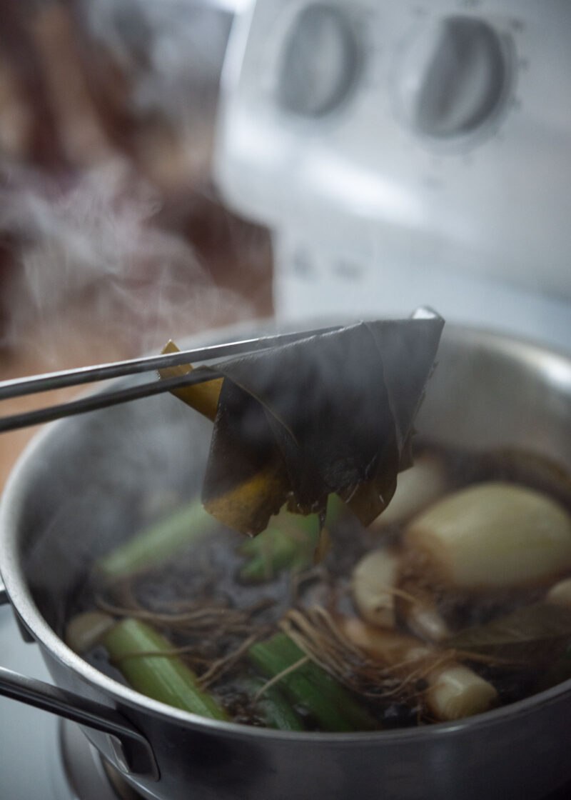 Removing kelp from a simmering soy marinade with onion, garlic, and green onions.