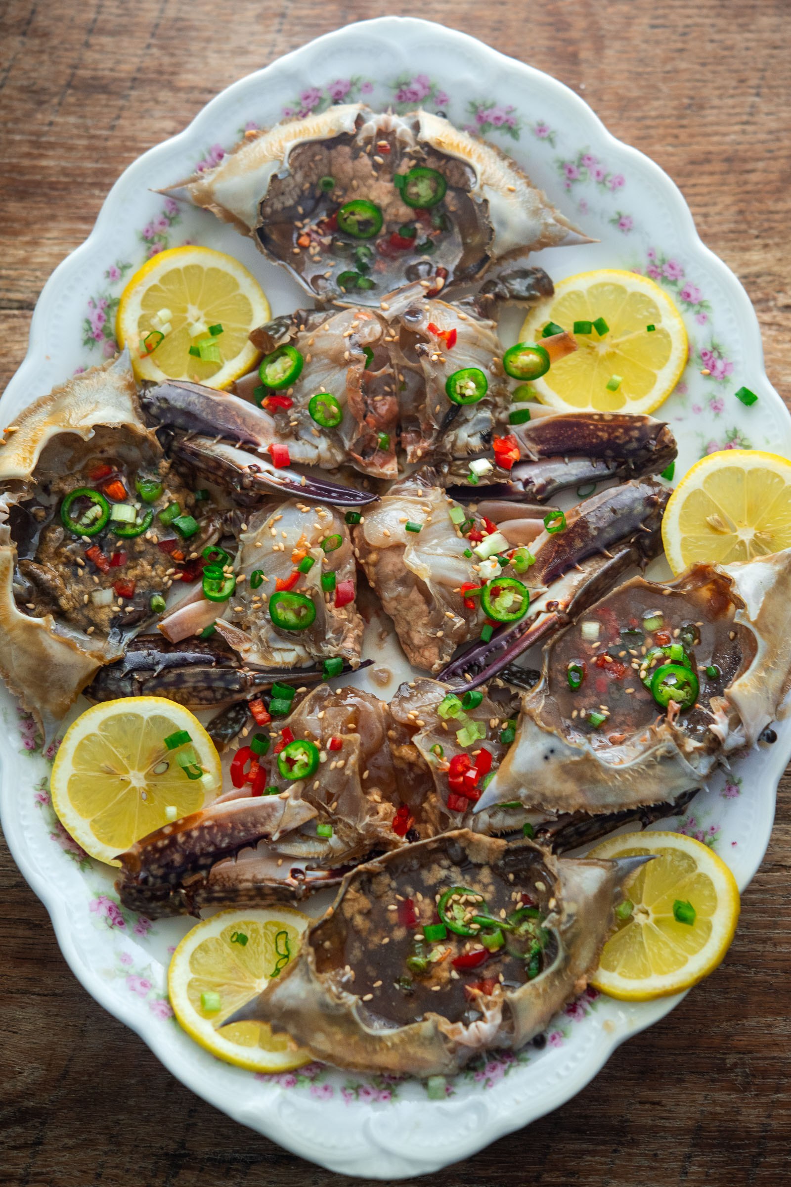 Ganjang gejang soy sauce-marinated crab on an oval platter with lemon slices, chopped green onions, and red chilies.
