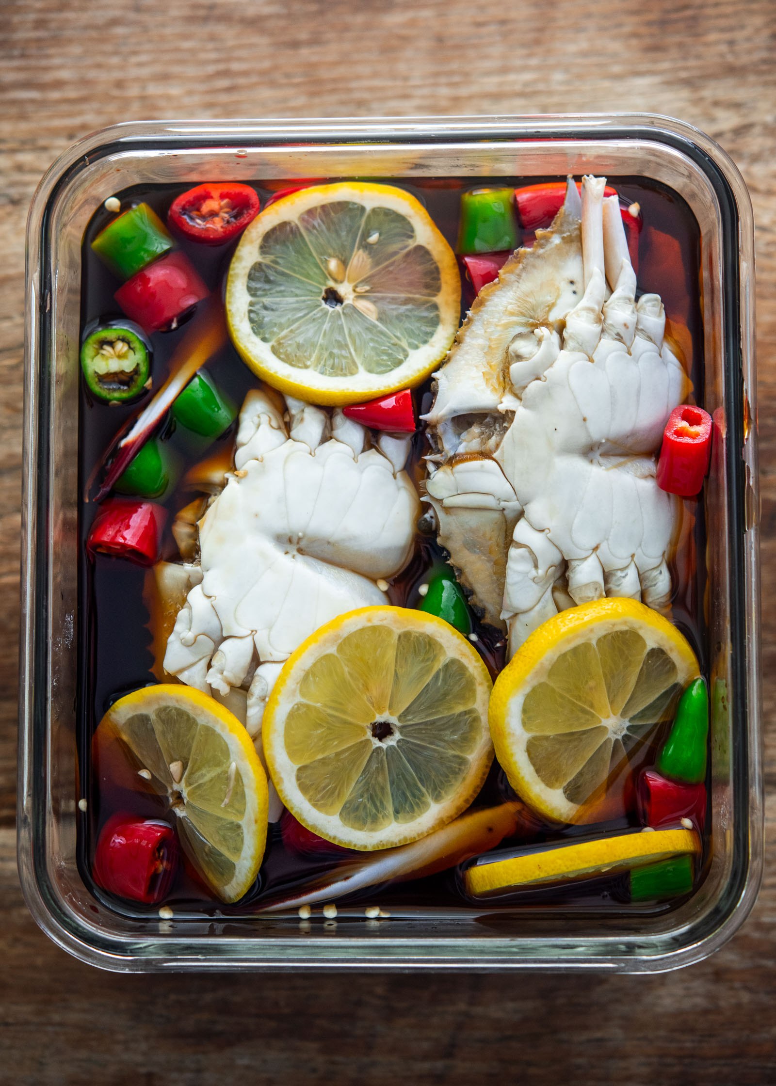 Soy-marinated crabs belly-side up with lemon slices and chilies in a glass container