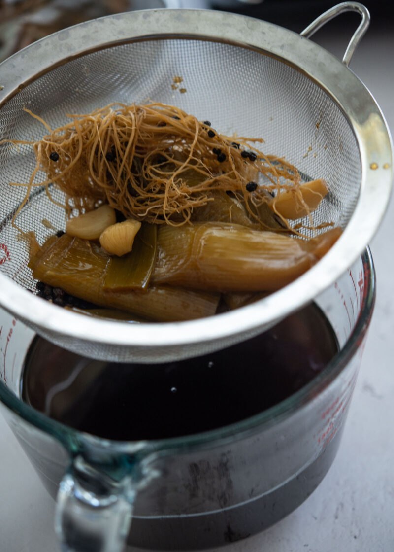 Straining onion, garlic, and daepa roots from the soy marinade.