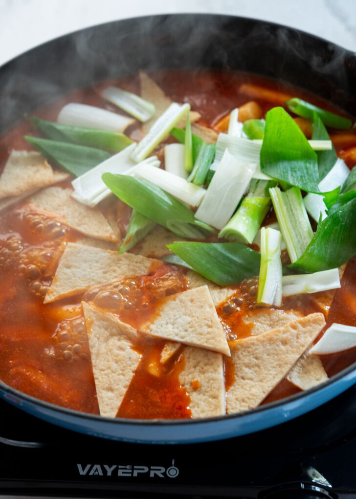 Adding fish cakes and leeks to simmering tteokbokki