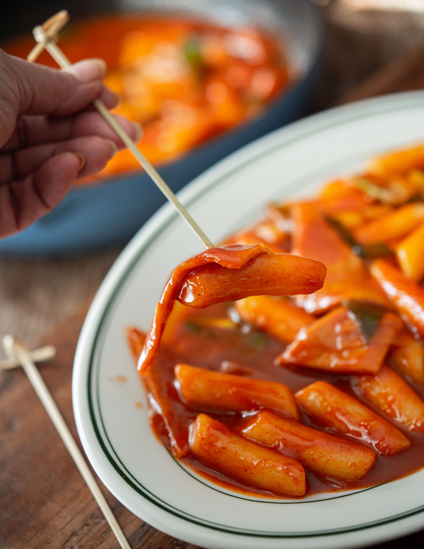 A toothpick picking up rice cake piece coated with spicy gochujang sauce