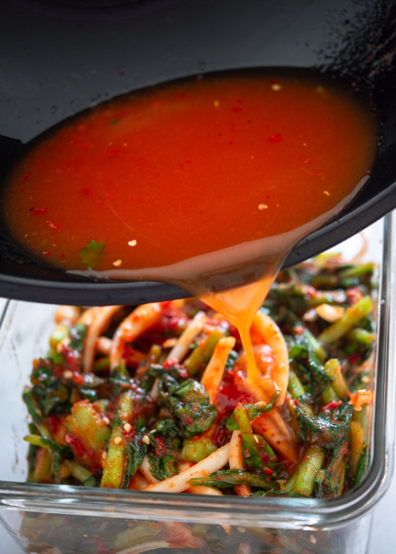 Pouring seasoned kimchi brine over yeolmu kimchi before fermentation