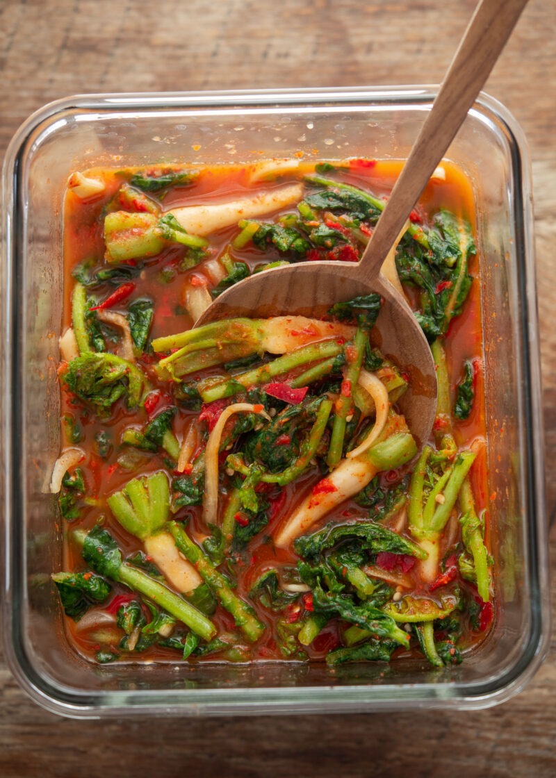 Yeolmu kimchi in a glass container with young radish greens and tangy red brine